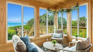 Una habitación con paneles de madera y ventanas amplias que dan a una playa y abundante vegetación.