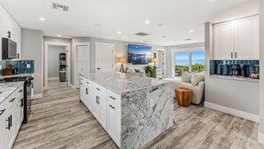 Una cocina moderna con una isla de mármol, armarios blancos y vistas al exterior.