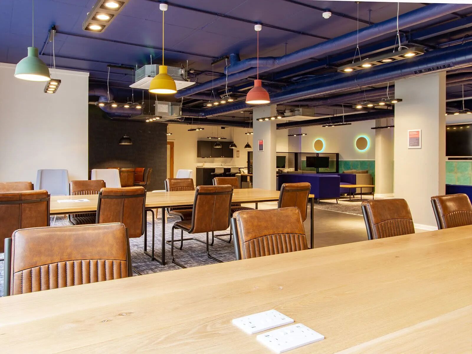 A modern conference room with wooden tables and leather chairs, equipped with pendant lighting and a large screen for presentations.