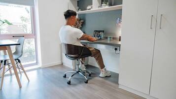 A person sitting at a desk in a room with a window, a chair, and a cabinet.