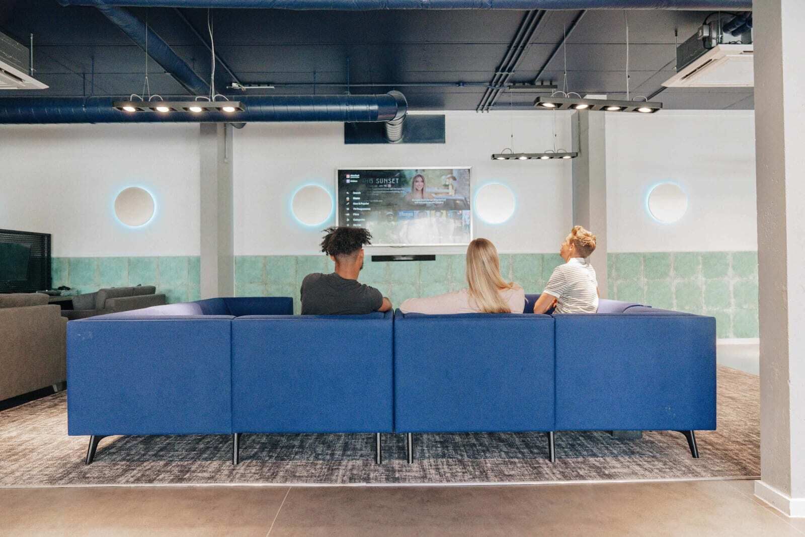A modern lounge area with a blue sofa, a flat-screen TV, and a wall-mounted screen displaying a video.