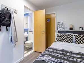 A bedroom with a bed, checkered pillows, a wooden door, and a bathroom visible through an open door.