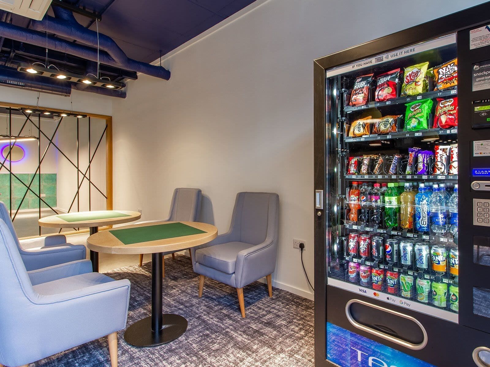 A modern lounge area with a pool table, comfortable seating, and a vending machine stocked with snacks and drinks.