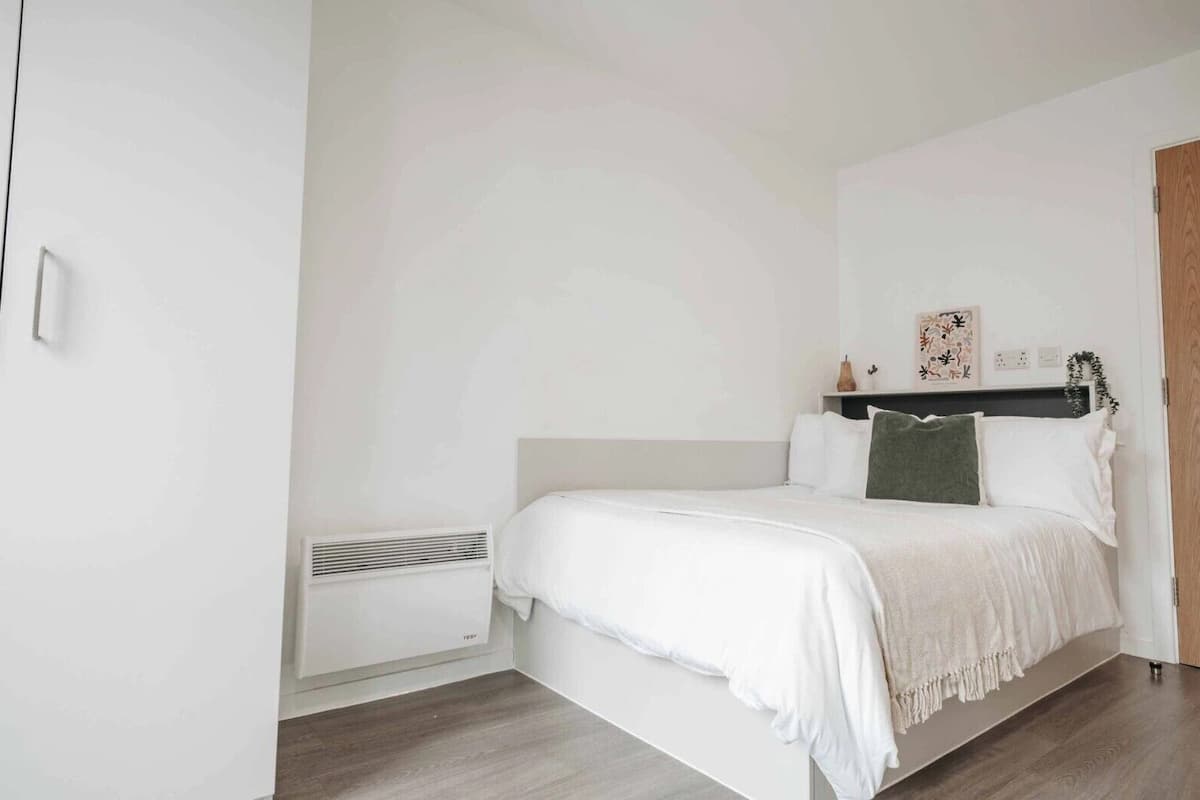 A minimalist bedroom with a bed, white walls, a wooden floor, and a small heater.