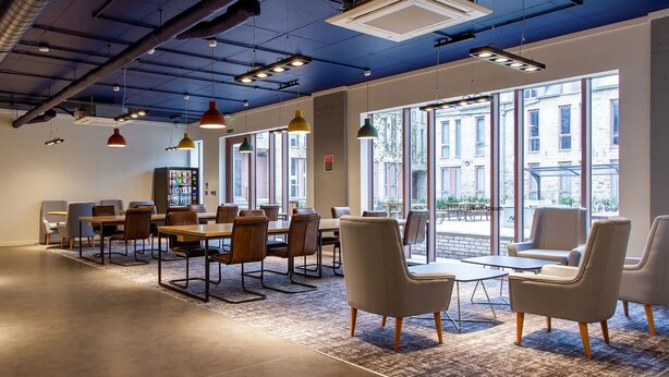 A modern office space with a large table and chairs, large windows, and industrial ceiling features. - Alma Court - Campus Accommodation (Canterbury)