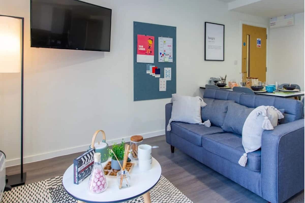 A modern living room with a flat-screen TV, a blue sofa, a coffee table with various items, and a bulletin board with papers.