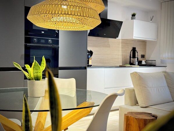 A modern kitchen with white cabinetry, a glass dining table, and a hanging light fixture.