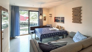 Ein modernes Wohnzimmer mit einer Couch, einem Esstisch mit gemustertem Tischläufer und Blick auf ein rotes Gebäude durch große Fenster.