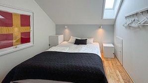 Ein Schlafzimmer mit einem Bett, Nachttischen, einem Kleiderschrank, einem Gemälde und einem Oberlicht.