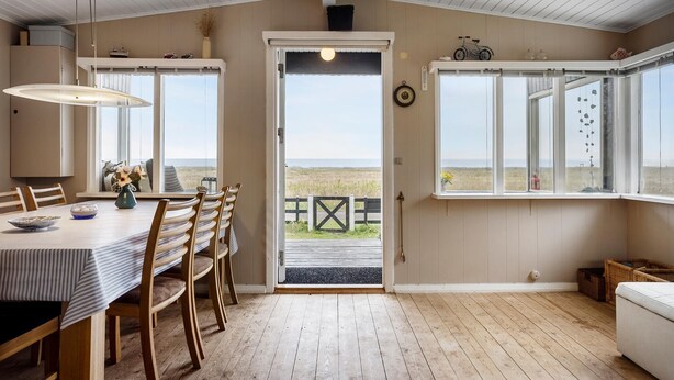 Un comedor con mesa y sillas, vista a la playa por una puerta, y una ventana con vista al mar.