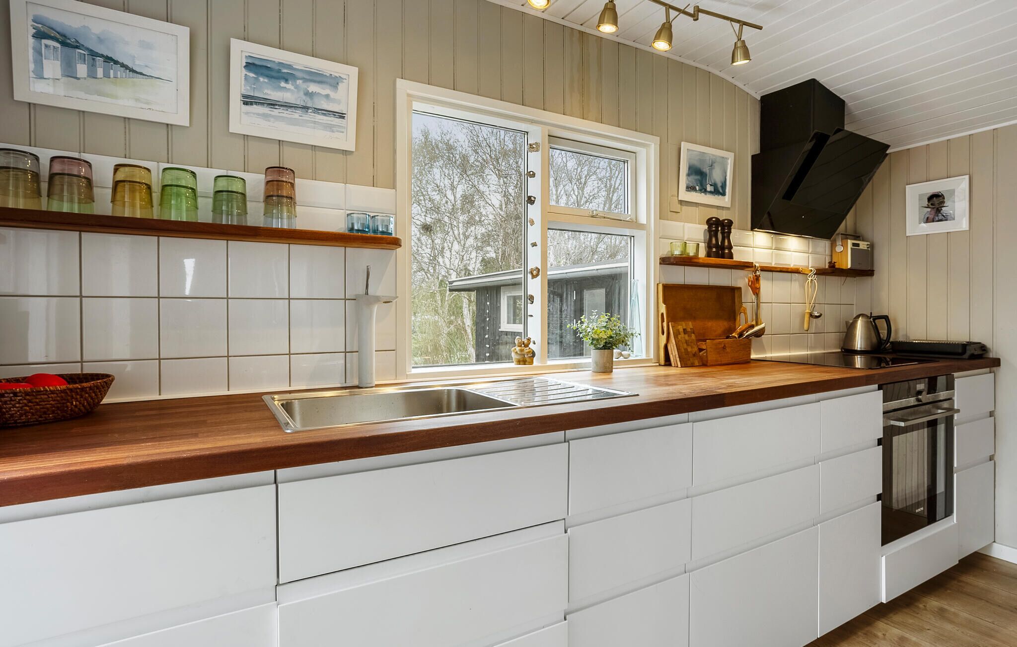 A modern kitchen with white cabinetry, a wooden countertop, and a large window providing a view of the outdoors.
