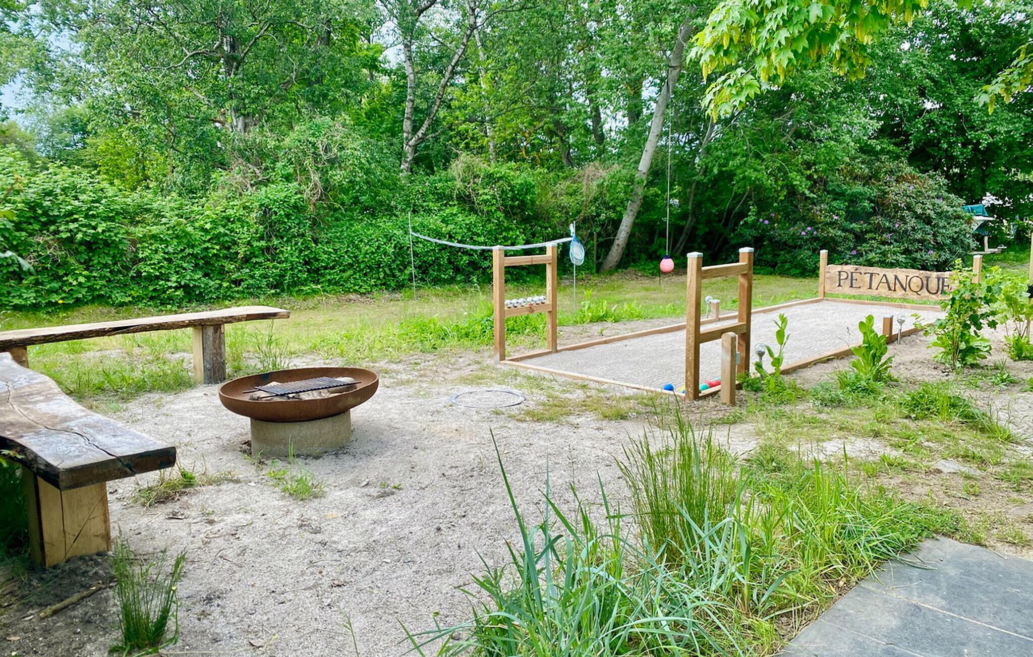 Un'area esterna rustica con una panchina di legno, un braciere e un cartello di legno con la scritta 'PÉTANQUE'.