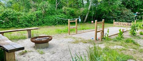 Un'area esterna rustica con una panchina di legno, un braciere e un cartello di legno con la scritta 'PÉTANQUE'.