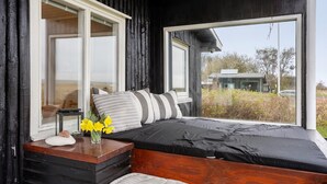 Un dormitorio acogedor con un ventanal grande, un cabecero de madera y una mesita de noche con un florero.