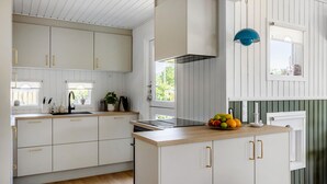 Una cucina moderna con mobili bianchi, maniglie dorate, un piano di lavoro in legno e una lampada a sospensione blu.