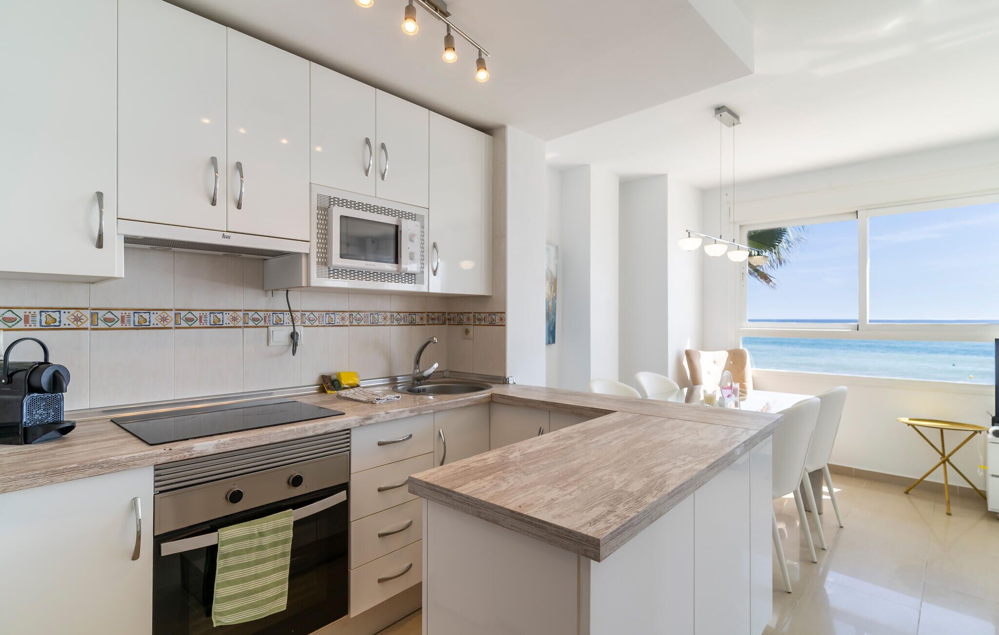 Una cocina moderna con armarios blancos, microondas y vista al océano.