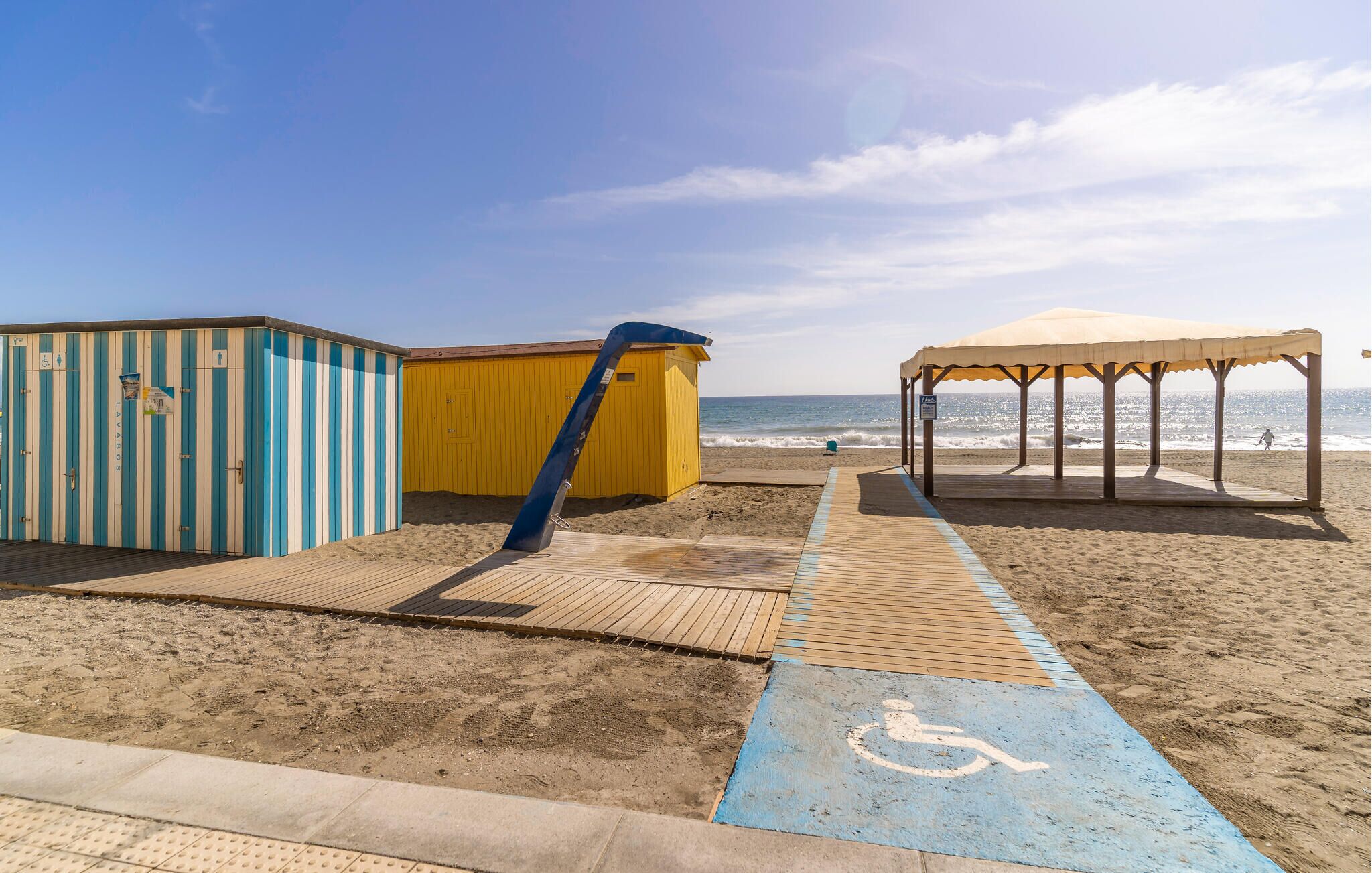 Ein Strand mit einem blau-weiß gestreiften Gebäude, einem gelben Gebäude und einer überdachten Laube.