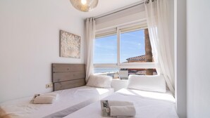 A hotel room with two beds, a large window with a view of the beach, and a painting on the wall. - Beach front apartment (San Luis de Sabinillas)
