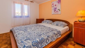A bedroom with a bed, a nightstand, a lamp, a wooden dresser, and a window with sheer curtains. - 1 bedroom beautiful apartment in Vir (Vir)