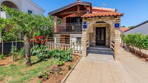 A two-story house with a stone entrance, a balcony, and a garden with red flowers. - 1 bedroom beautiful apartment in Vir (Vir)