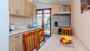 A compact kitchen with wooden cabinets, a built-in oven, and a dining area with a table set for two. - 1 bedroom beautiful apartment in Vir (Vir)