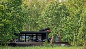 A modern outdoor dining area with a built-in table and chairs, surrounded by lush greenery and trees.