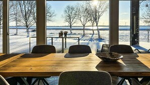 A dining area with a wooden table and chairs, a bowl, and a view of a snowy landscape with trees and wind turbines.