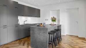 A modern kitchen with grey cabinets, a central island with stools, and a herringbone wooden floor.
