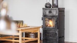 A room with a wood-burning stove, a chessboard, and a table.