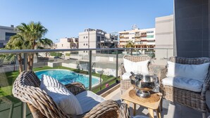 Un balcon agrémenté de meubles en osier, une piscine et une vue sur le paysage urbain.