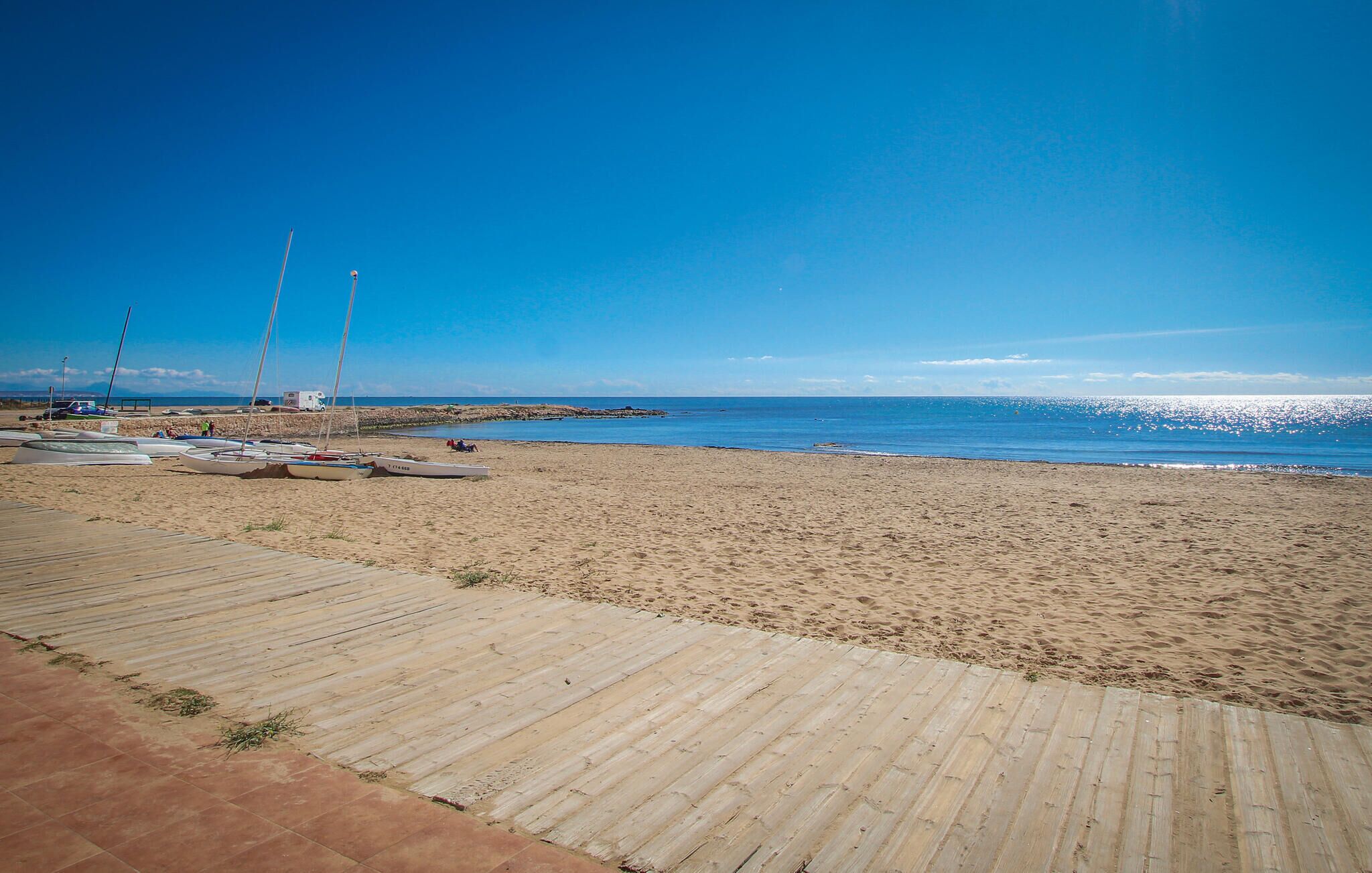 Ein sandiger Strand mit einer Holzpromenade, die zum Wasser führt.