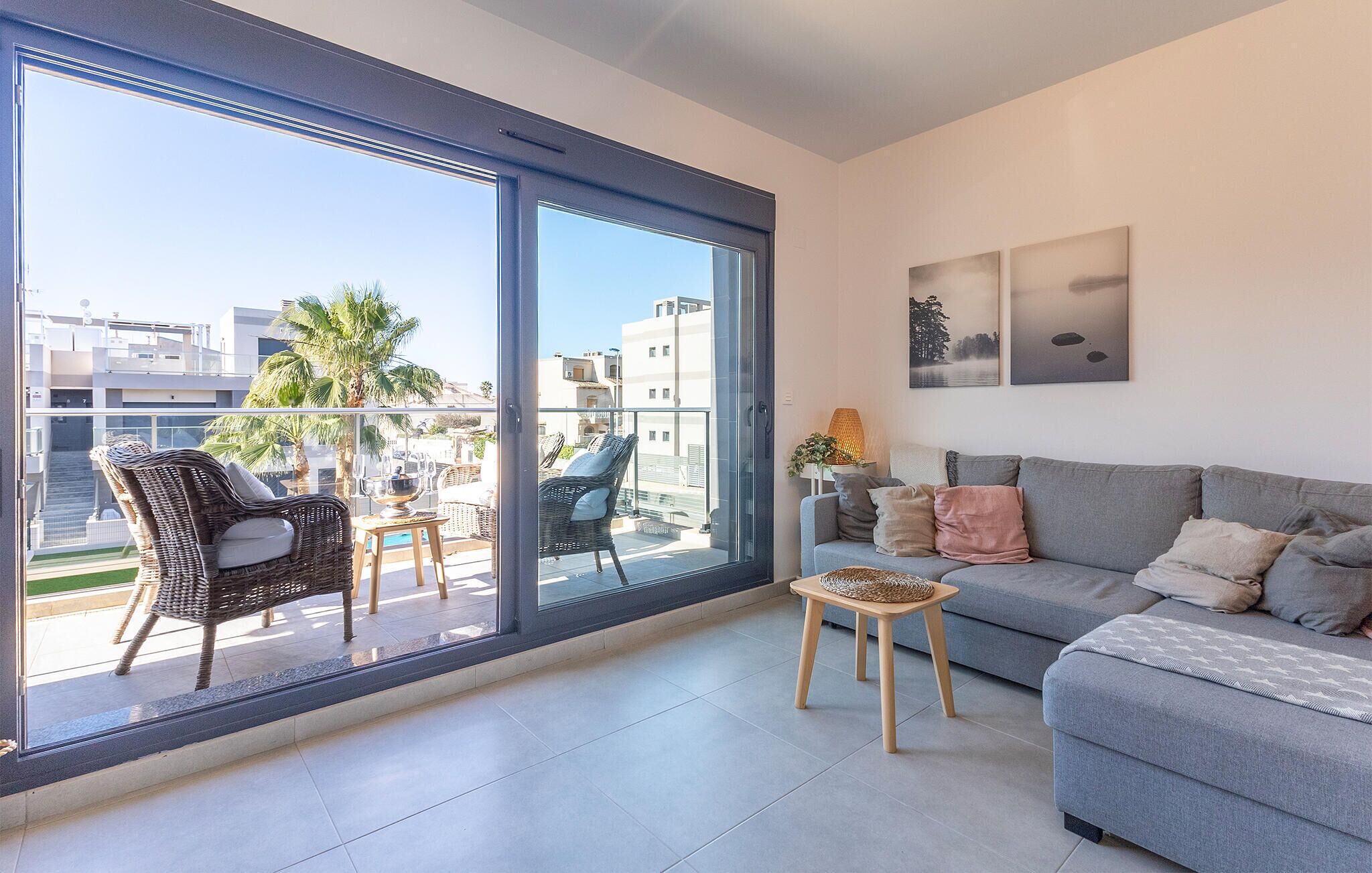 A modern apartment with a balcony, a grey sofa, wicker chairs, and a small table.