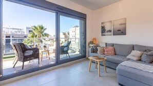 Un appartement moderne doté d’un balcon, d’un canapé gris, de fauteuils en osier et d’une petite table.