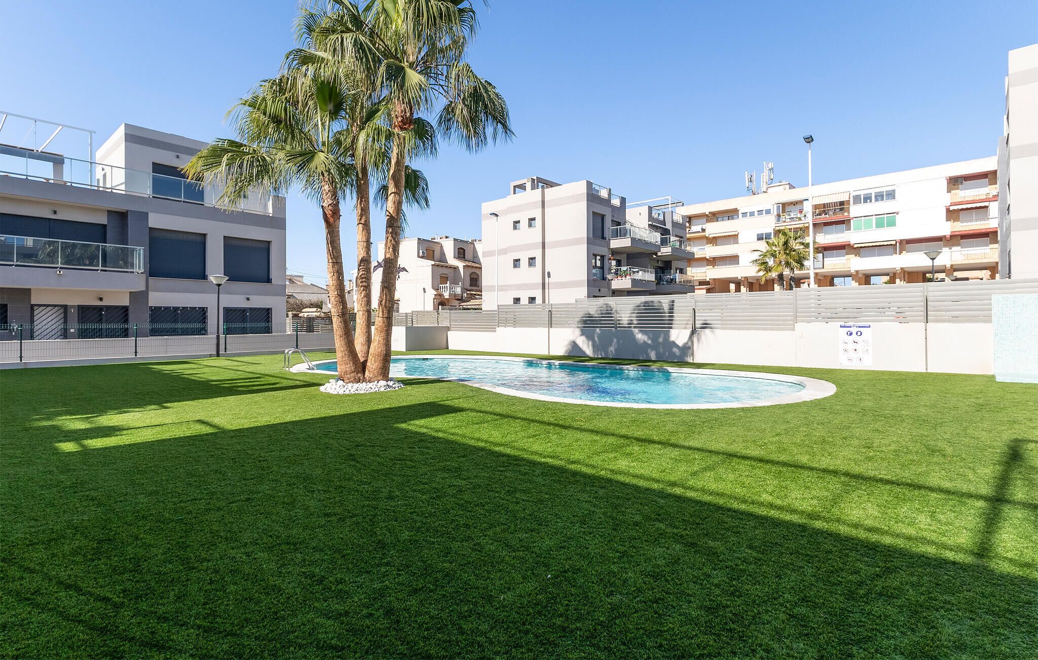 A modern residential area with a swimming pool, palm trees, and multi-story buildings.