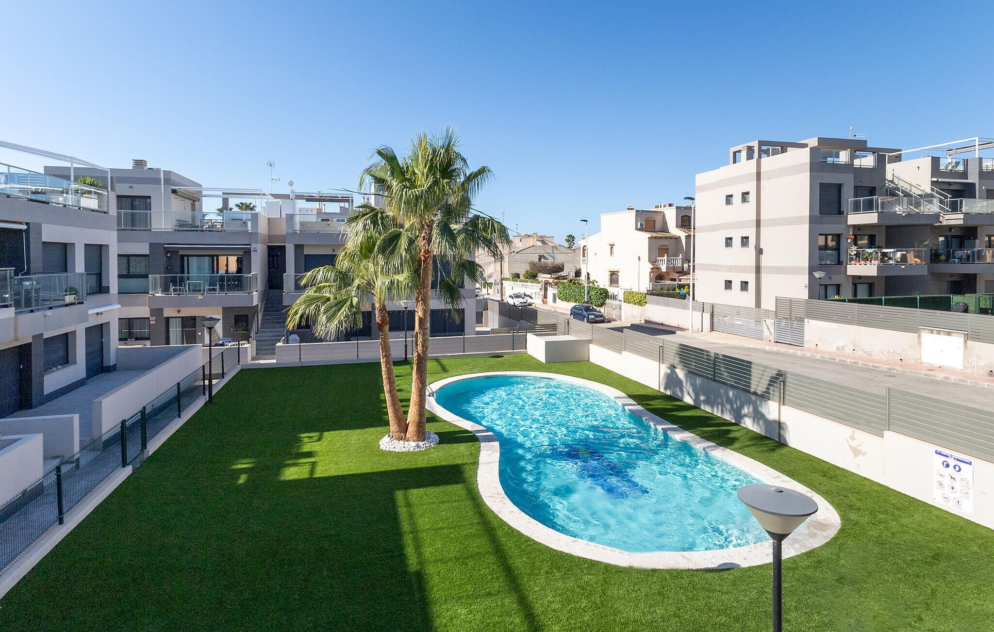 A modern apartment complex with a swimming pool, palm trees, and a well-maintained lawn.