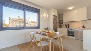 Une cuisine moderne avec des meubles blancs, un réfrigérateur en acier inoxydable et un coin repas comprenant une table et des chaises.