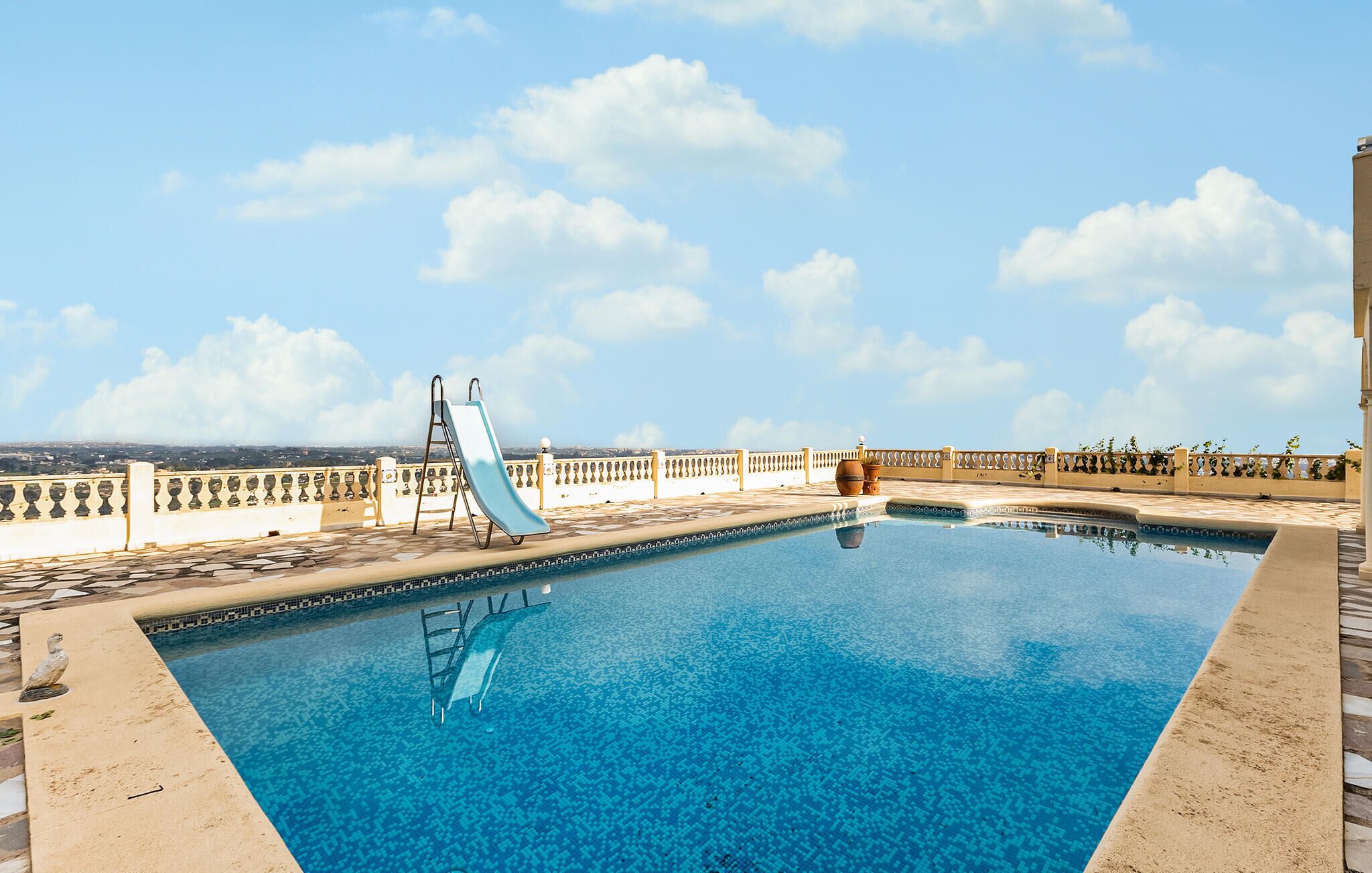 Ein Swimmingpool mit Rutsche, umgeben von einer gefliesten Terrasse und einem dekorativen Zaun.