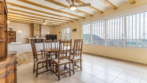 A spacious dining area with a high ceiling and exposed beams, a stone fireplace, and large windows offering a city view. - Amazing home in Denia (Denia)
