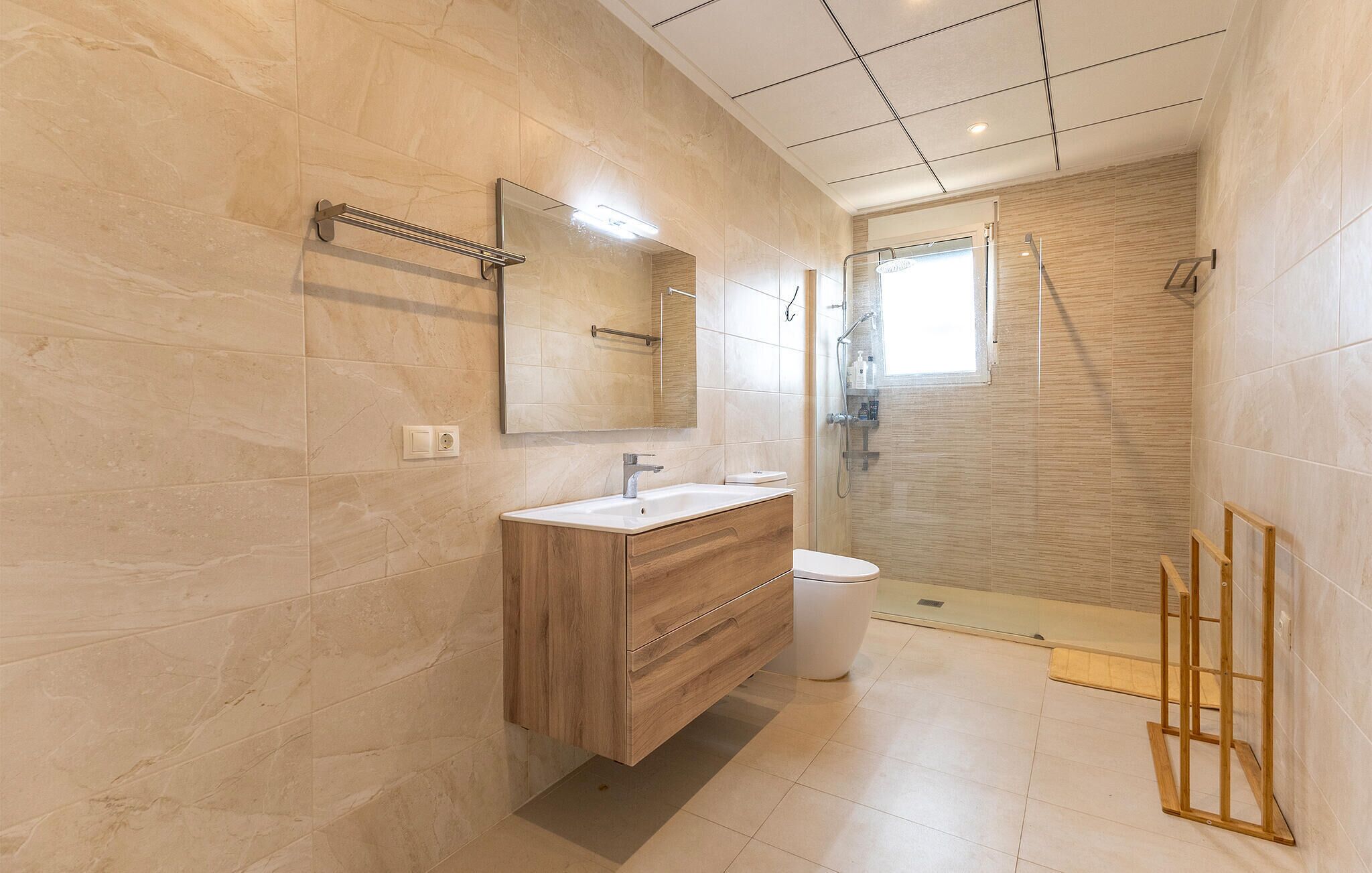 A modern bathroom with a wooden vanity, a mirror, a toilet, and a shower area.