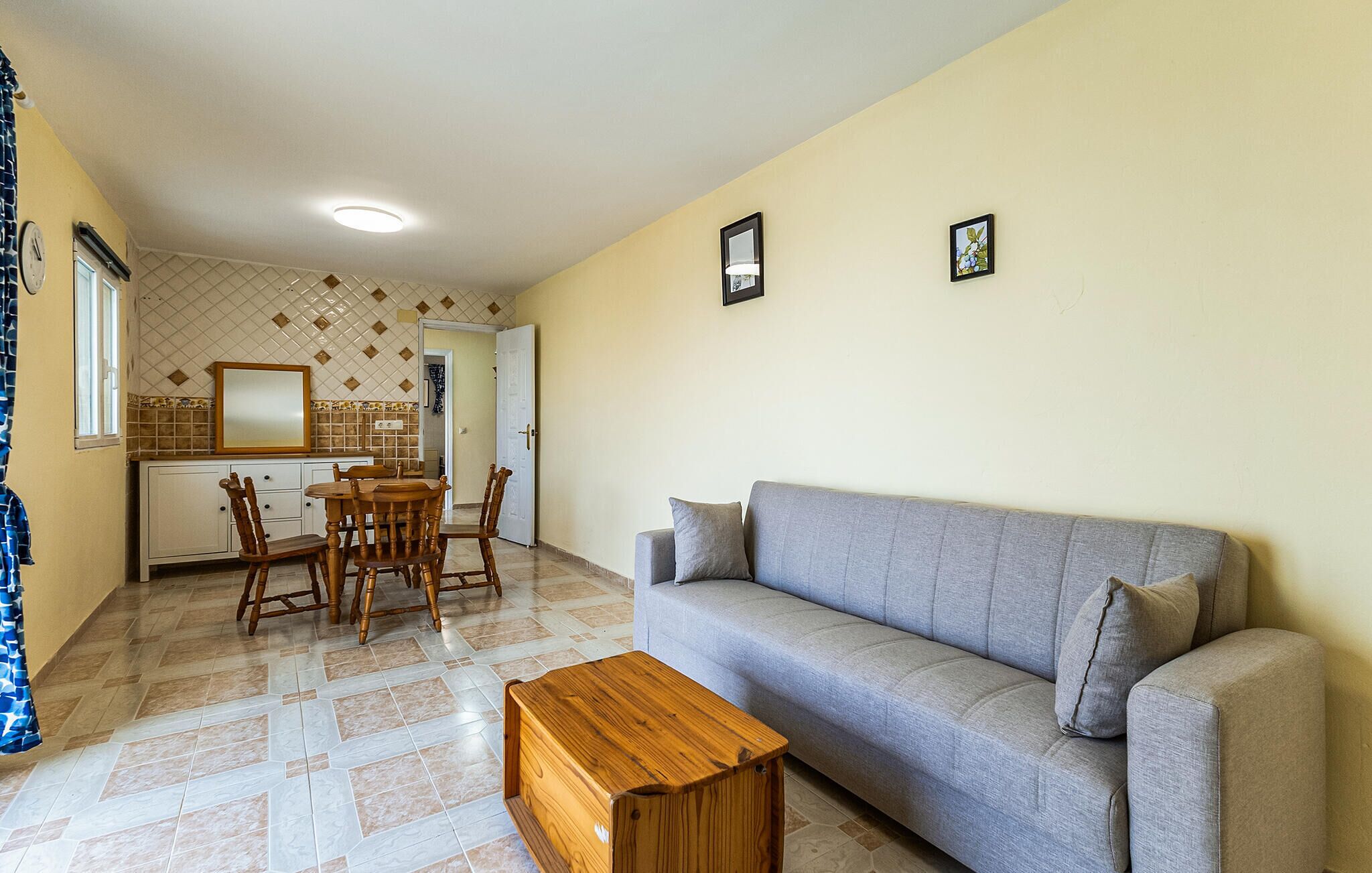 A living room with a grey sofa, wooden coffee table, and a dining area with a wooden table and chairs.