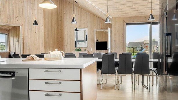 Una cocina moderna con encimera blanca, electrodomésticos de acero inoxidable y un comedor con sillas negras y un amplio ventanal.