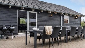 Un patio exterior con mesa y sillas, una parrilla y una construcción de madera con techo de tejas.