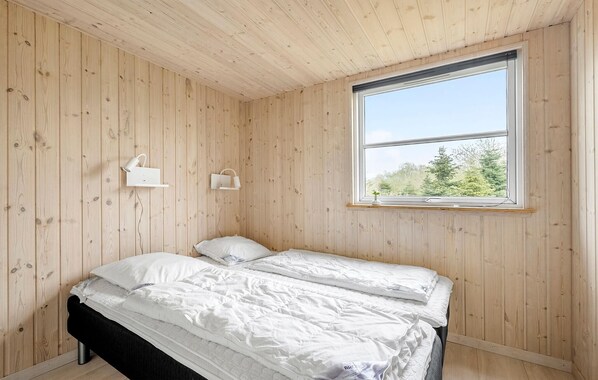 A bedroom with wooden walls, a large window, a bed with white bedding, and two bedside tables with lamps.