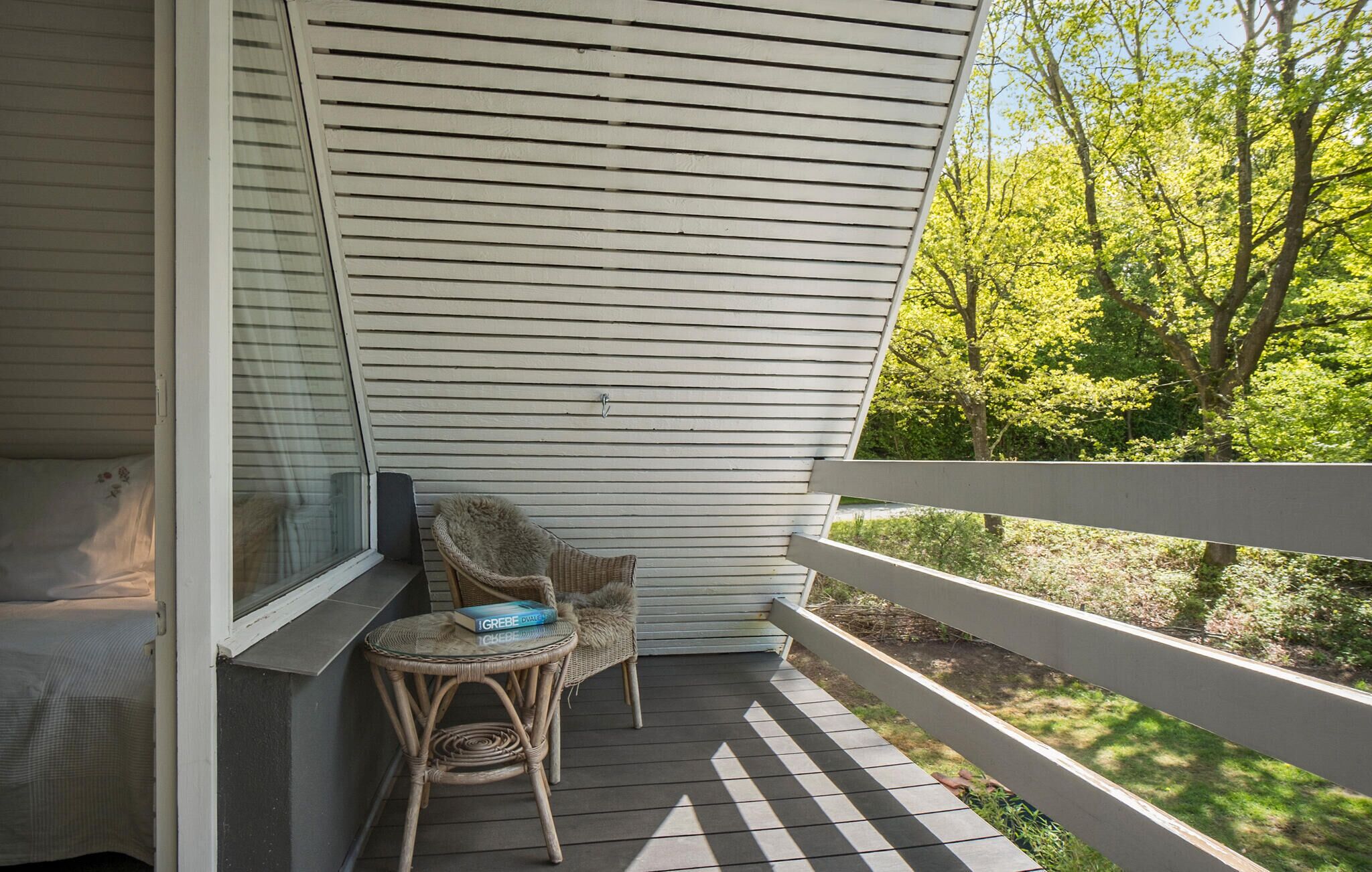 A covered porch with two wicker chairs and a small table, overlooking a wooded area.