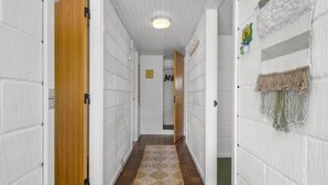 En hall med vit tegelvägg, trädörrar, en vävd matta och en taklampa.
