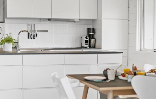 Una cocina moderna con muebles blancos, un lavamanos de acero inoxidable y una cafetera.