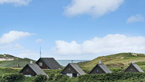En række traditionelle træhuse med saddeltage, foran en klar himmel og et fjernt havblik.