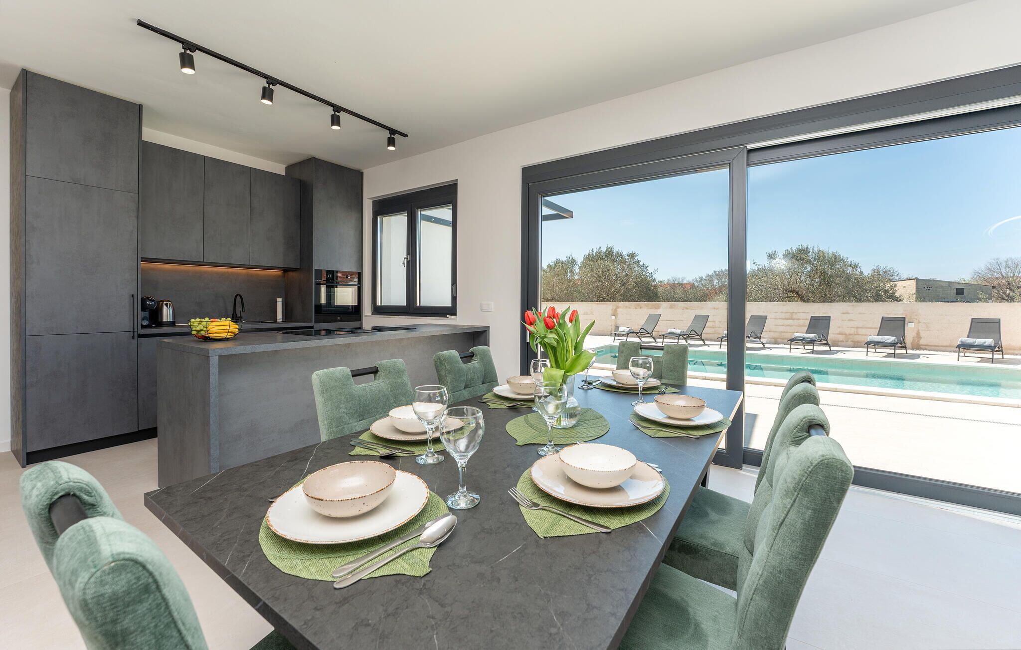 A modern kitchen with dark cabinets, a dining area with a table set for four, and a poolside view.