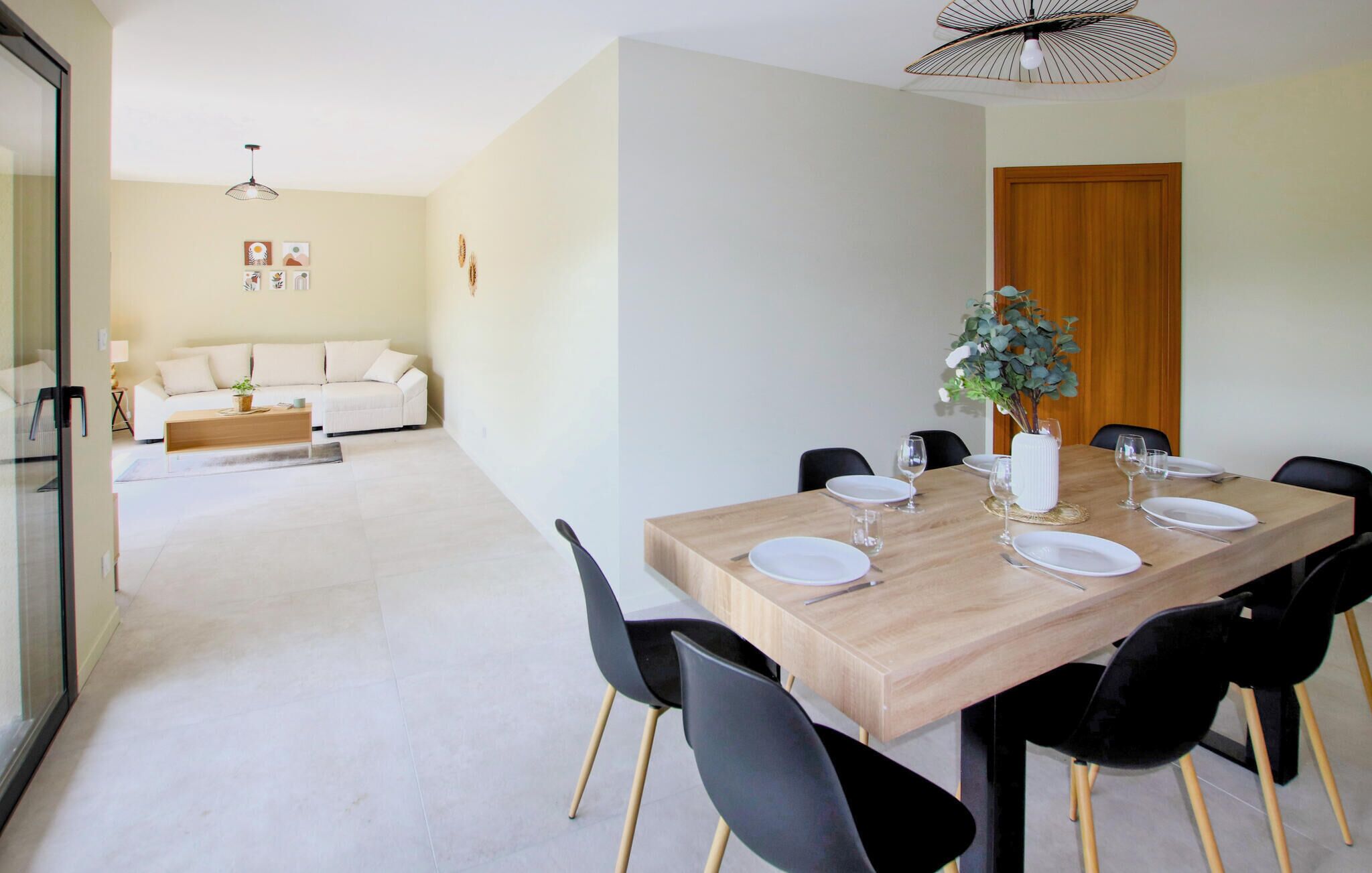 A dining area with a wooden table set for four, black chairs, and a vase with greenery.