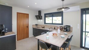 A modern kitchen with a wooden door, a built-in stove, a coffee machine, and a dining area with a table and chairs. - Lovely home in Puy St Martin (Puy St Martin)